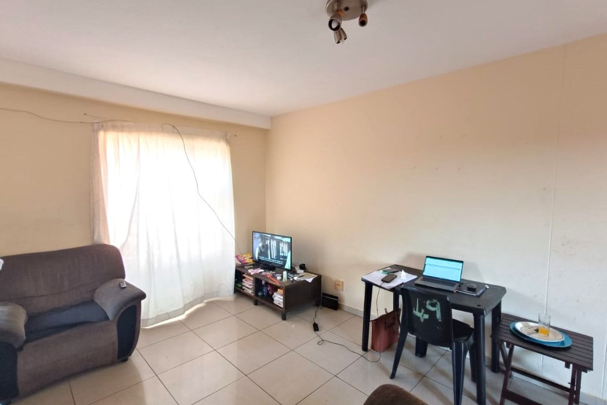 A living room area featuring tiled flooring and a ceiling-mounted spotlight fixture, offering a functional space with potential for cosmetic updates.