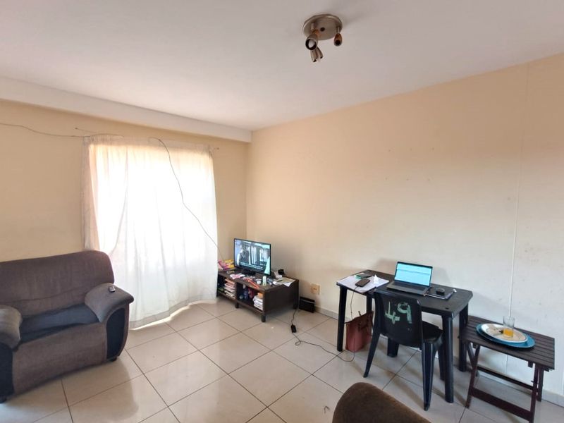 A living room area featuring tiled flooring and a ceiling-mounted spotlight fixture, offering a functional space with potential for cosmetic updates.