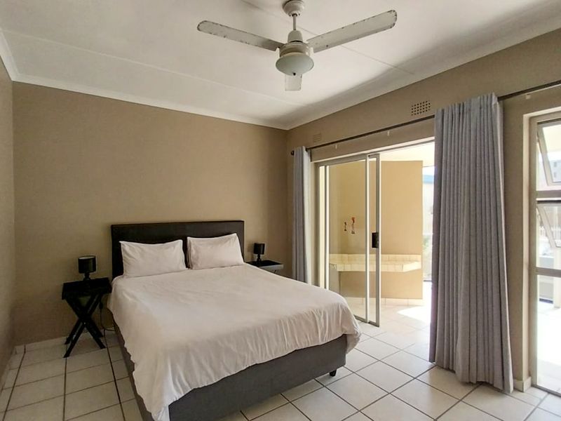 A bedroom featuring tiled flooring, a ceiling fan, and sliding glass doors that provide access to an outdoor balcony area.