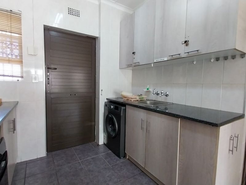 Functional kitchen featuring built-in cabinetry, granite countertops, a stainless steel sink, and tiled finishes with direct access to an external door.
