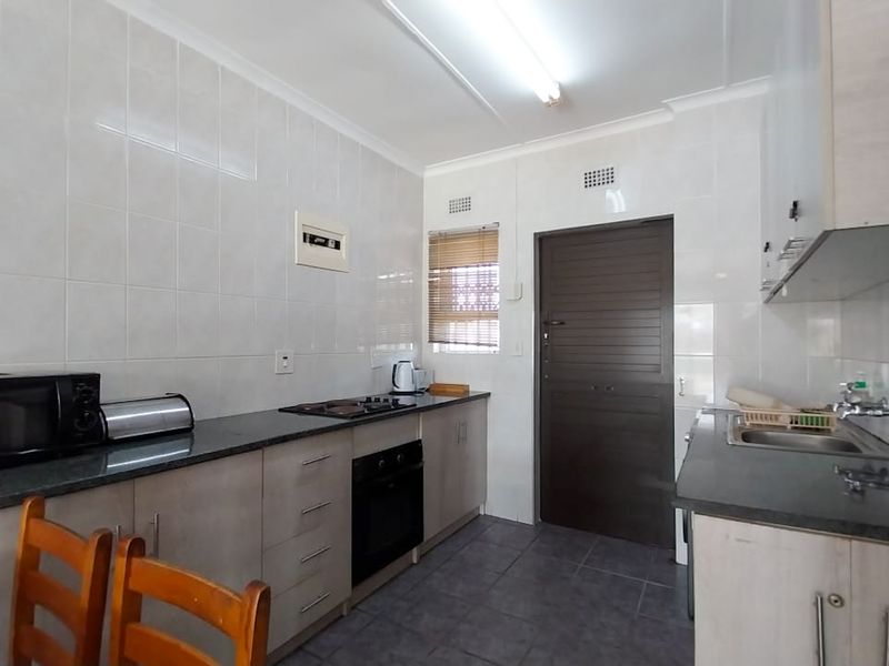 A functional kitchen featuring built-in cabinetry, laminate countertops, a built-in oven, hob, and tiled splashbacks with durable floor tiling.