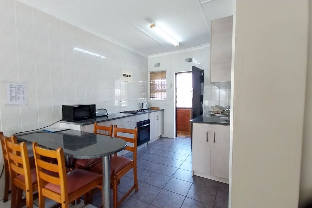 A functional kitchen featuring tiled walls and flooring, built-in cabinetry, a hob, and an oven, with direct access to an exterior area.