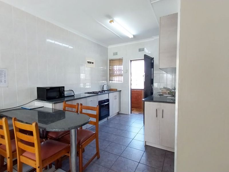 A functional kitchen featuring tiled walls and flooring, built-in cabinetry, a hob, and an oven, with direct access to an exterior area.