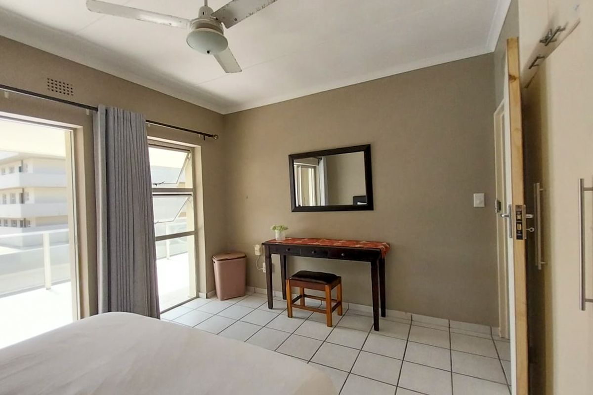 A bedroom featuring tiled flooring, a ceiling fan, built-in cupboards, and a sliding glass door providing access to an outdoor balcony area.