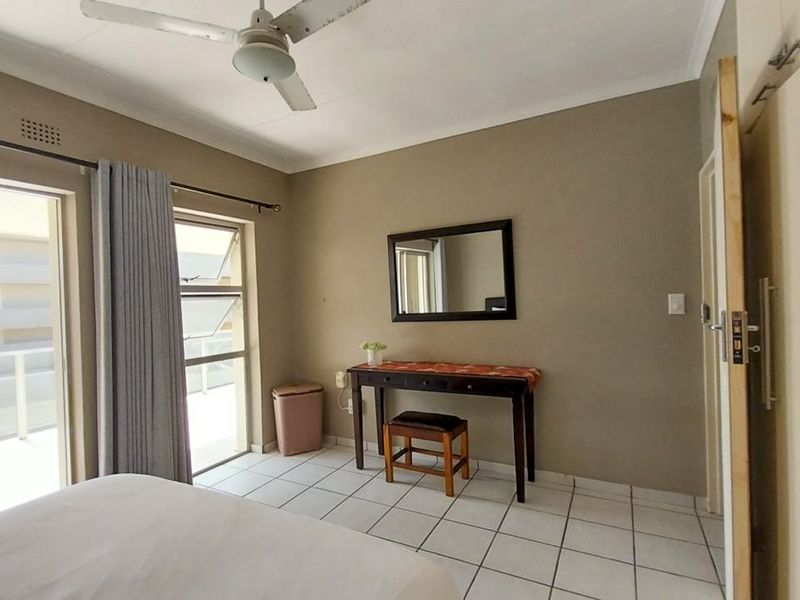 A bedroom featuring tiled flooring, a ceiling fan, built-in cupboards, and a sliding glass door providing access to an outdoor balcony area.