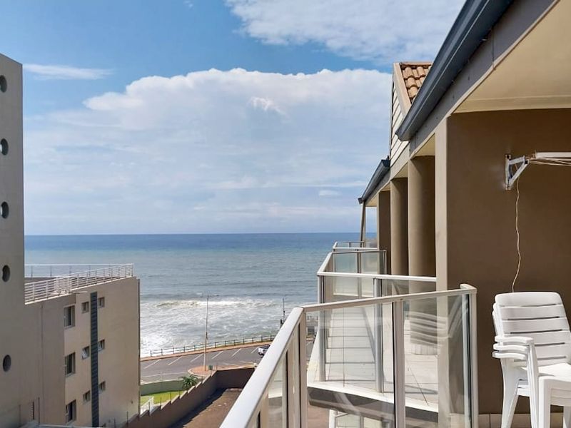 A spacious balcony featuring a glass balustrade and tiled flooring, offering expansive ocean views and a convenient wall-mounted drying rack.