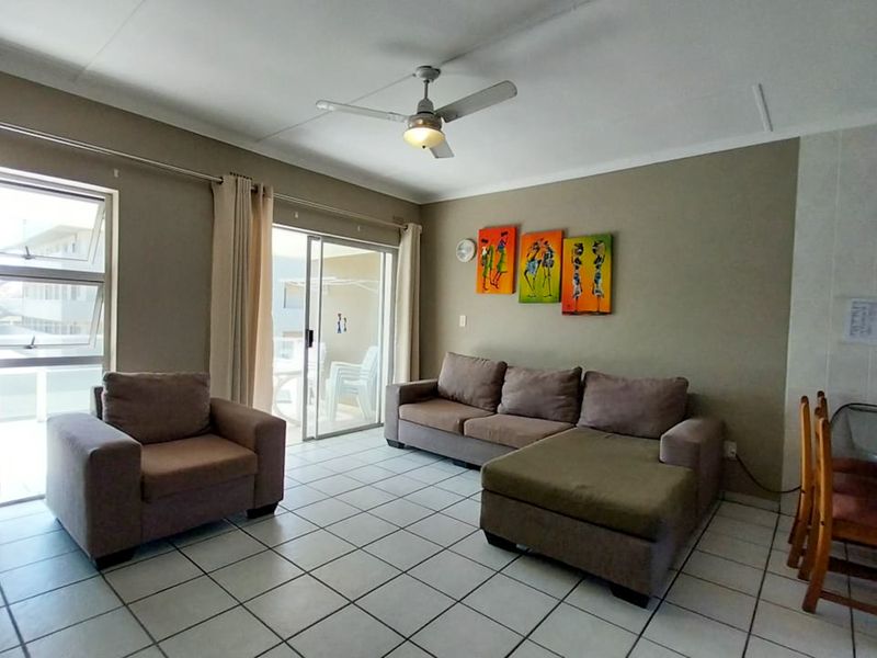 Open plan living area featuring tiled flooring, a ceiling fan, and sliding glass doors providing access to an outdoor patio space.