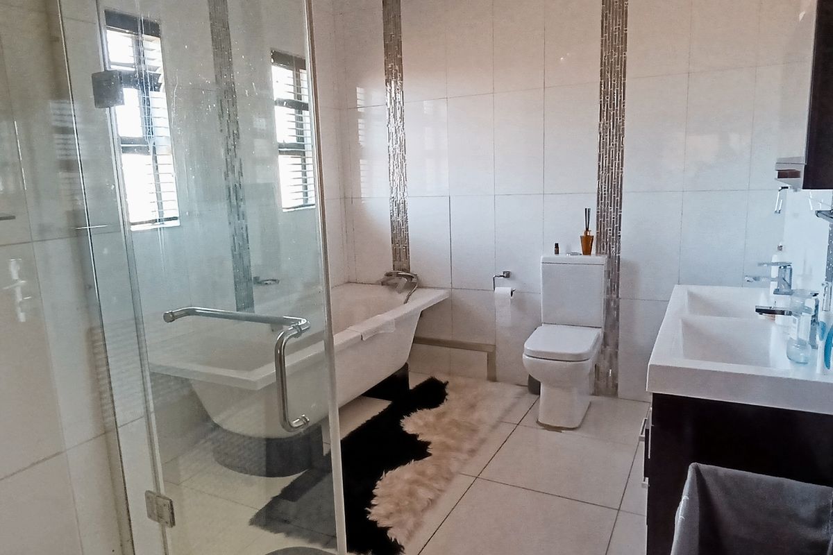 Modern bathroom featuring a freestanding bathtub, glass-enclosed shower, double vanity, and contemporary wall-mounted toilet with stylish mosaic tile accents.
