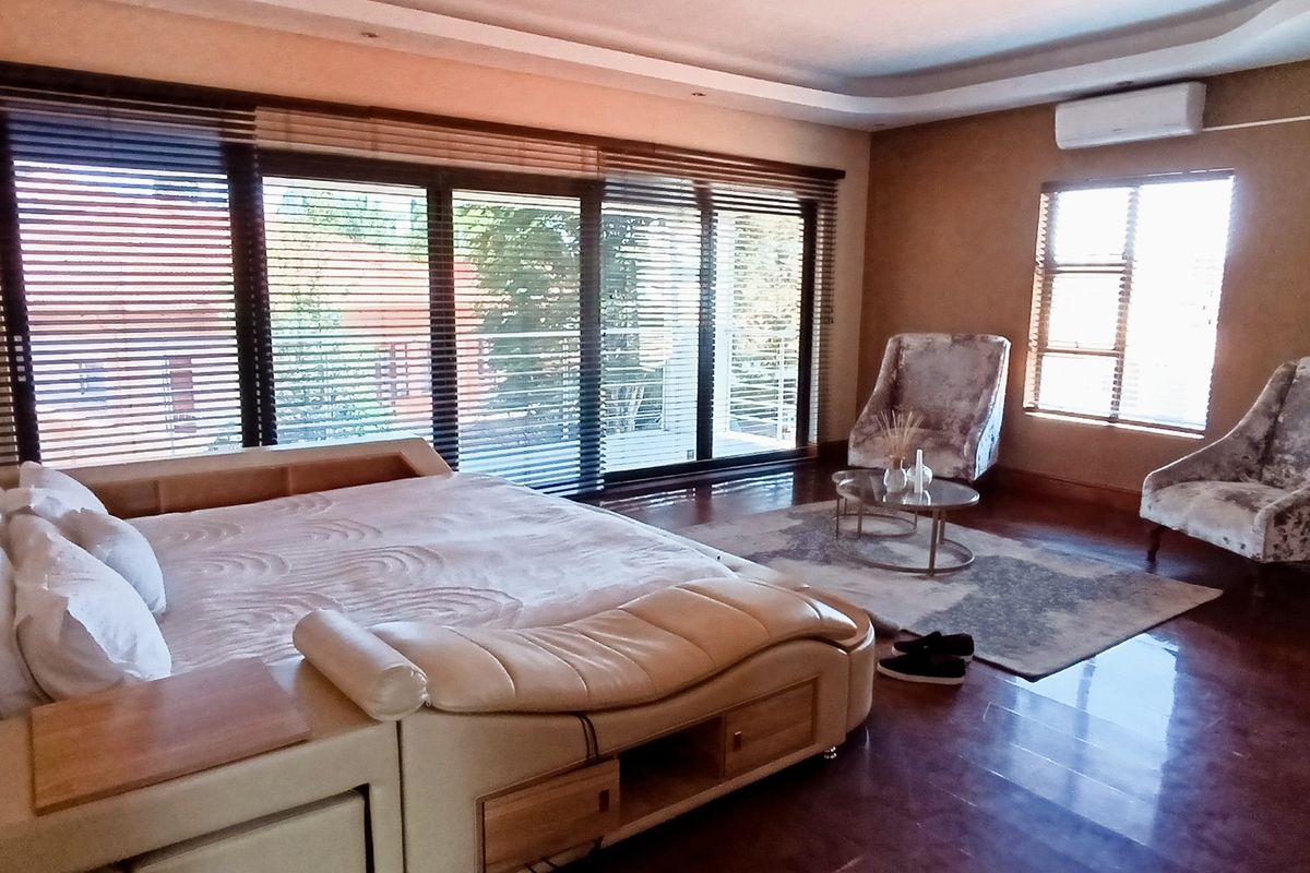 Spacious bedroom featuring hardwood flooring, recessed ceiling lighting, a wall-mounted air conditioning unit, and large sliding glass doors with venetian blinds.