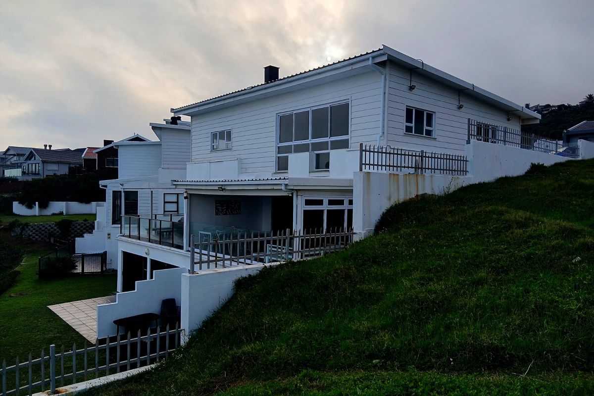 Rear exterior view of a multi-level townhouse featuring white cladding, a covered patio area, glass balustrades, and a sloped garden.