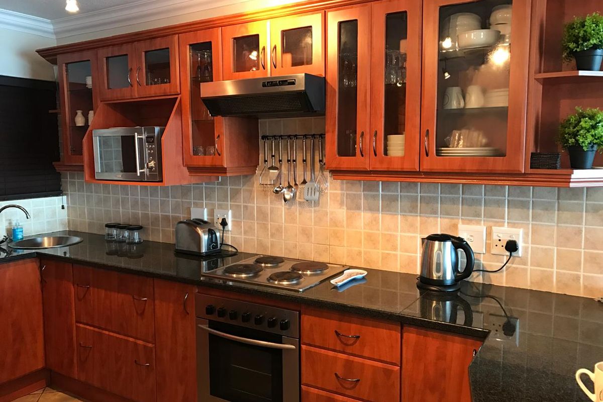 A functional kitchen featuring warm-toned wooden cabinetry, dark granite countertops, a built-in oven, electric hob, and an integrated extractor fan.