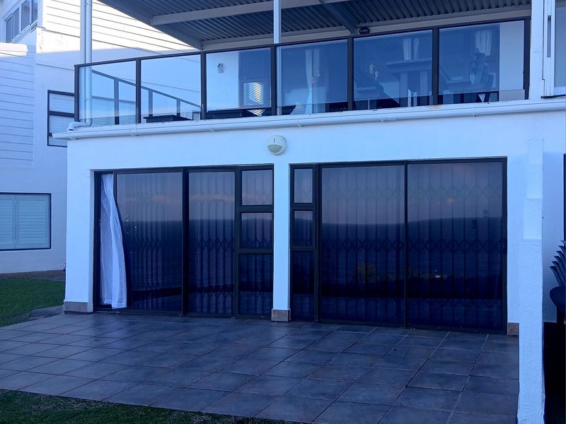A two-level townhouse exterior featuring a ground-floor tiled patio and an upper-level balcony with glass balustrades and a covered roof structure.