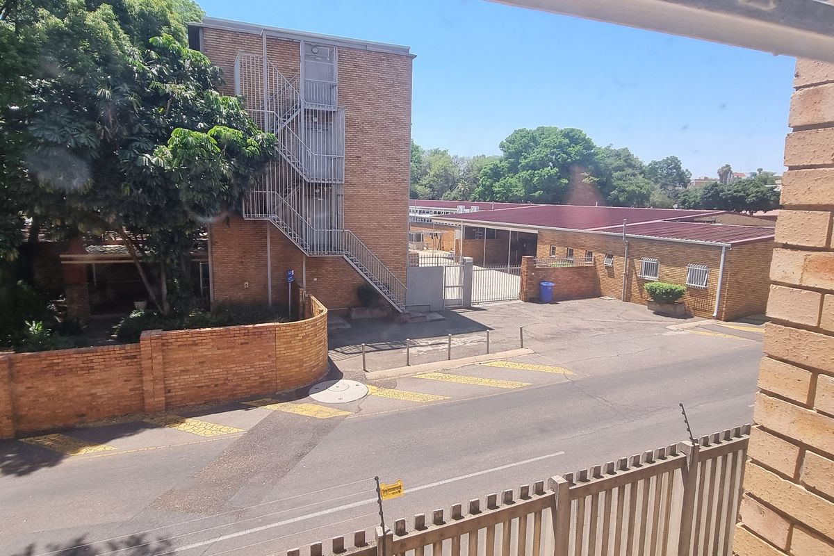 An elevated view of the property's rear exterior, featuring a paved driveway, brick boundary walls, and an external metal staircase.