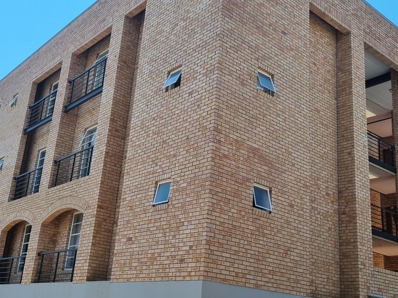 A multi-story apartment building featuring a face brick facade, metal balcony railings, and modern casement windows.