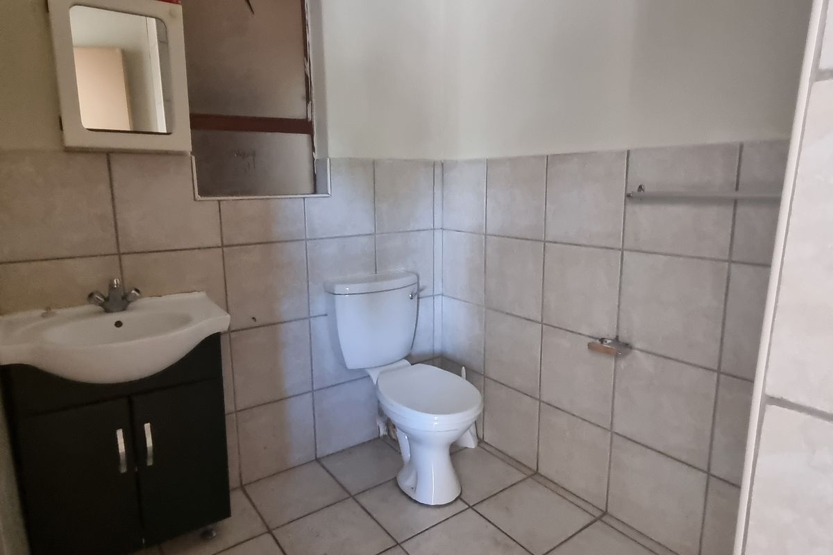 A functional bathroom featuring a vanity cabinet, ceramic basin, and toilet, finished with neutral wall and floor tiles.