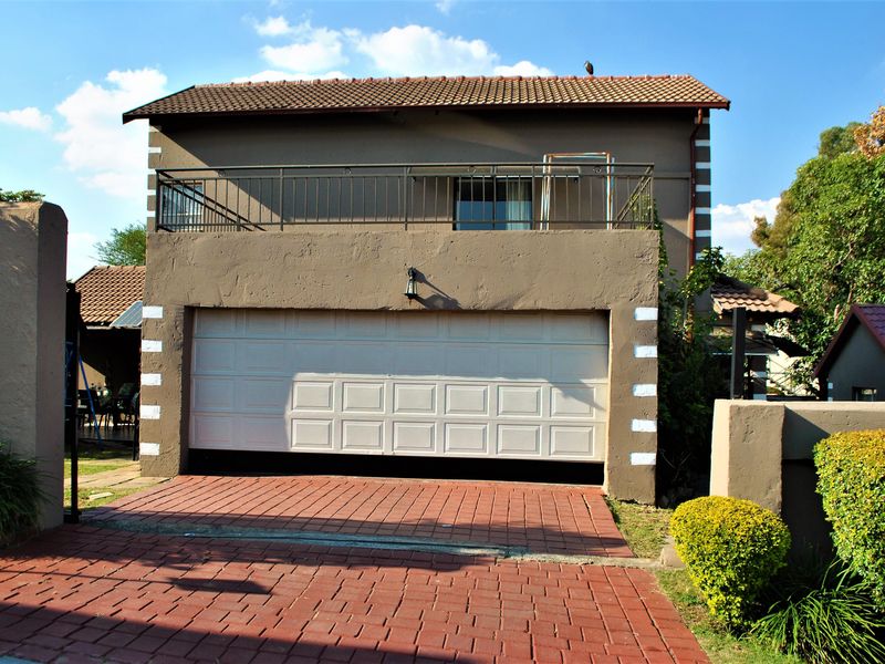 Front elevation of a two-story house featuring a double garage, a paved driveway, and an upper-level balcony with metal railings.