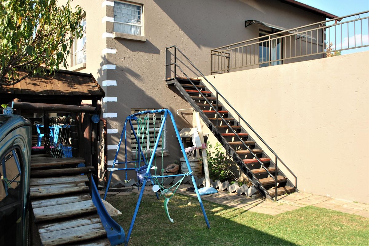 Rear exterior view of the property featuring a metal staircase leading to an upper balcony and a paved garden area.