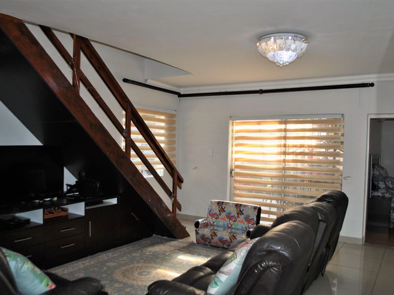 Living room featuring a wooden staircase with integrated storage, tiled flooring, and sliding glass doors with roller blinds providing natural light.