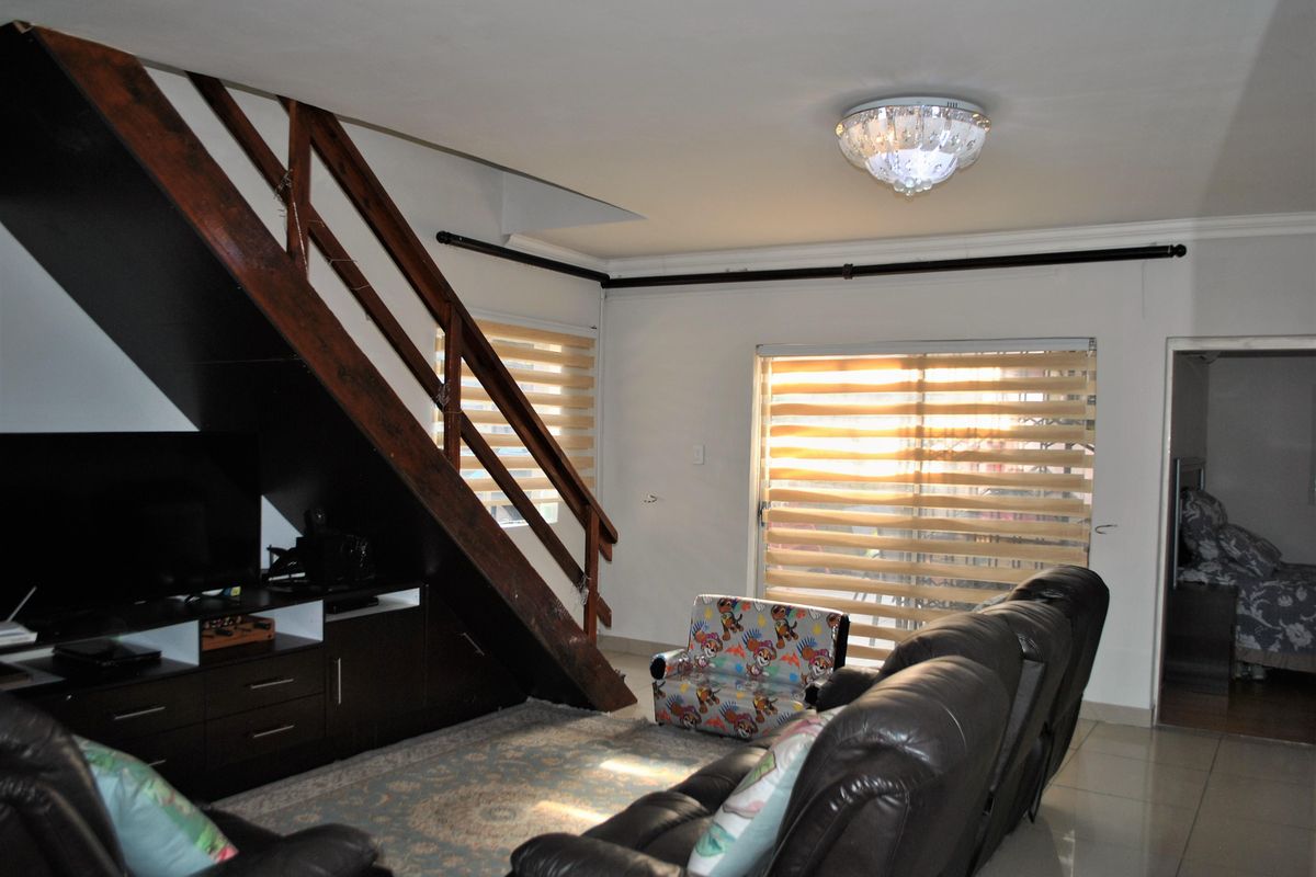 Living room featuring a wooden staircase with integrated storage, tiled flooring, and sliding glass doors with roller blinds providing natural light.