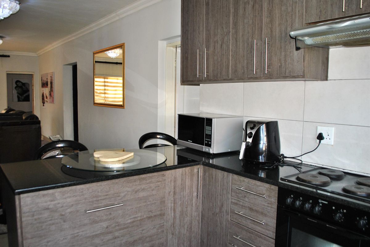 A functional kitchen featuring modern wood-grain cabinetry, black granite countertops, and integrated appliances including an electric hob and oven.