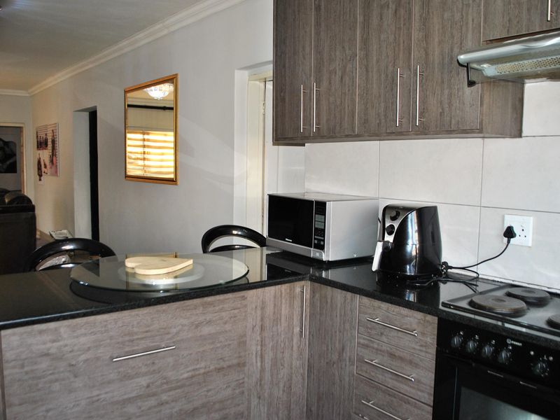 A functional kitchen featuring modern wood-grain cabinetry, black granite countertops, and integrated appliances including an electric hob and oven.