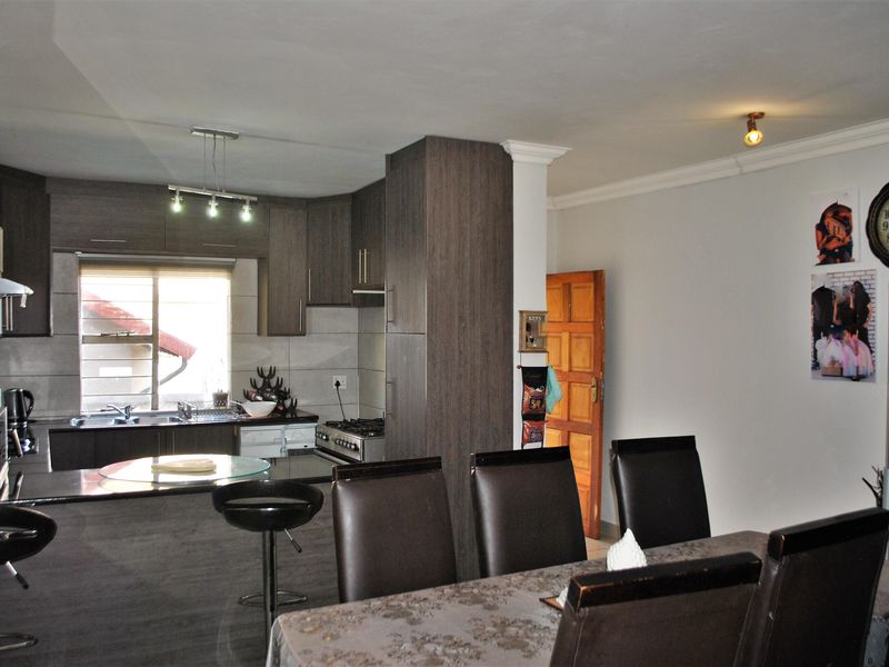 Open-plan kitchen and dining area featuring modern dark wood cabinetry, granite countertops, and a built-in gas stove with an integrated extractor fan.
