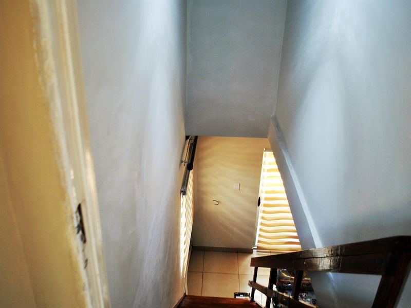 A functional staircase area featuring tiled flooring, a wooden handrail, and roller blinds, providing access between levels.