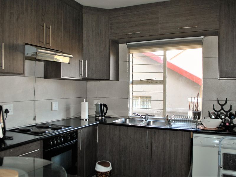 A functional kitchen featuring dark wood-grain cabinetry, granite countertops, a built-in electric stove with extractor fan, and a stainless steel sink.