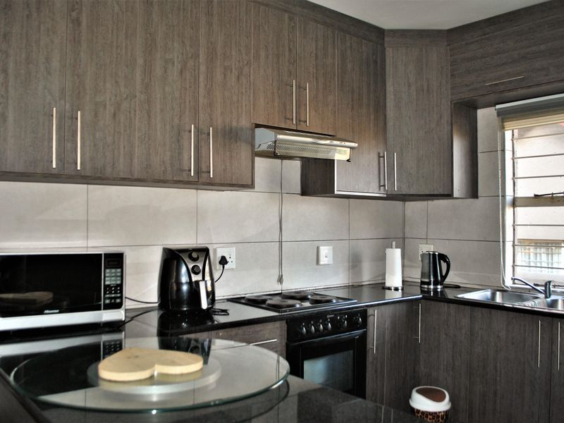 Modern kitchen featuring dark wood-grain cabinetry, granite countertops, integrated appliances, and a tiled backsplash with ample storage space.