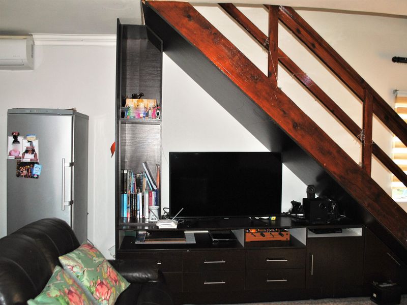 Living area featuring custom built-in cabinetry under a wooden staircase, air conditioning unit, and window blinds.