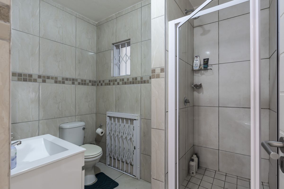 A functional bathroom featuring a walk-in shower with glass enclosure, a vanity basin, and a toilet, finished with neutral wall and floor tiling.