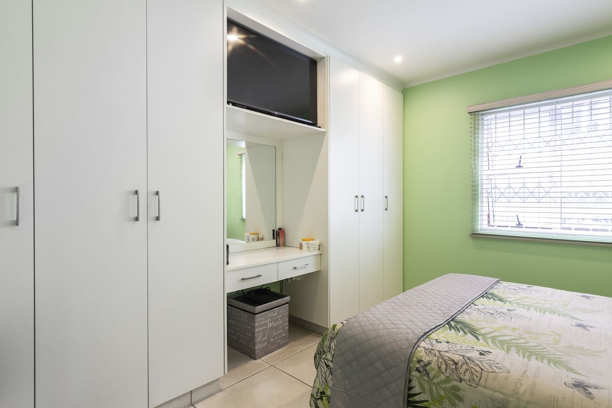 A well-maintained bedroom featuring extensive built-in white cabinetry, a integrated vanity station, and tiled flooring with a bright green accent wall.