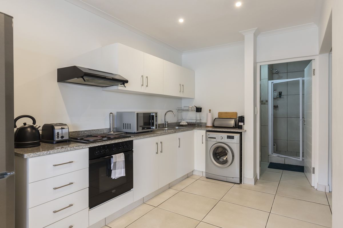 Modern kitchen featuring white cabinetry, granite countertops, built-in oven, hob, extractor fan, and integrated laundry space, with an adjacent bathroom visible.