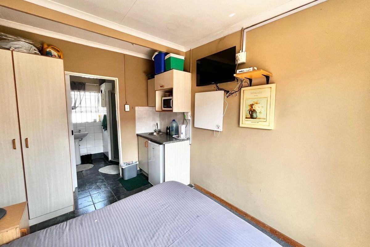 Compact studio bedroom featuring a small kitchenette area with built-in cabinetry and an adjoining bathroom with tiled flooring.