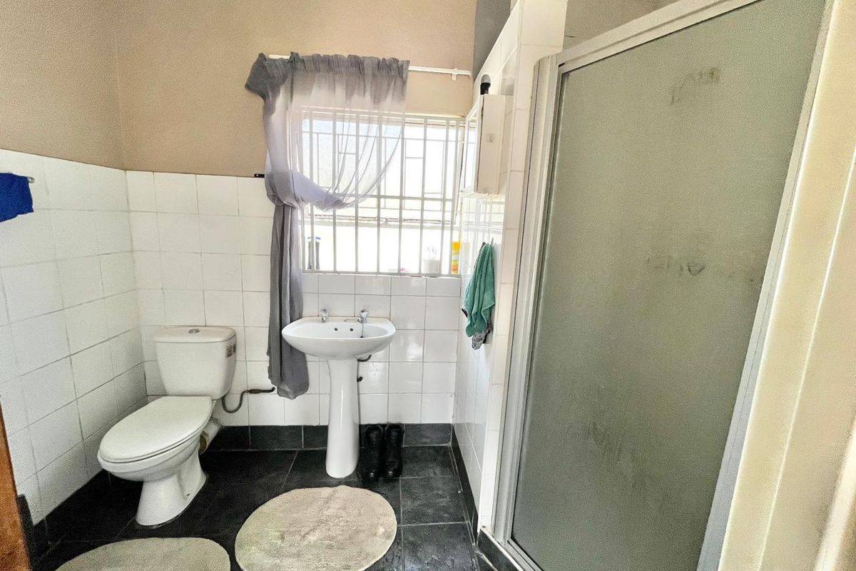 A functional bathroom featuring a pedestal sink, a standard toilet, and a glass-enclosed shower stall with tiled walls and dark floor tiling.