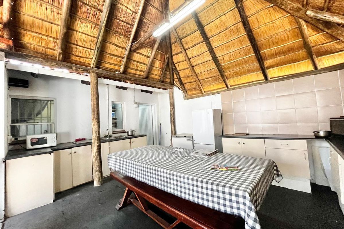 Rustic kitchen area featuring a high vaulted thatch ceiling, built-in cabinetry, tiled splashbacks, and a central dining space.