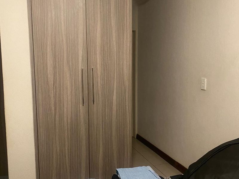 A bedroom featuring a modern wood-grain built-in wardrobe, tiled flooring, and decorative coving.