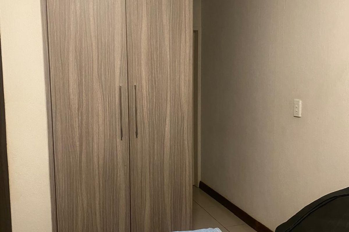 A bedroom featuring a modern wood-grain built-in wardrobe, tiled flooring, and decorative coving.