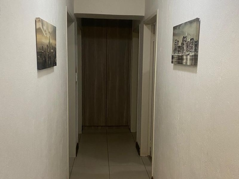 A functional hallway featuring tiled flooring, crown molding, and a built-in cupboard at the end of the passage.