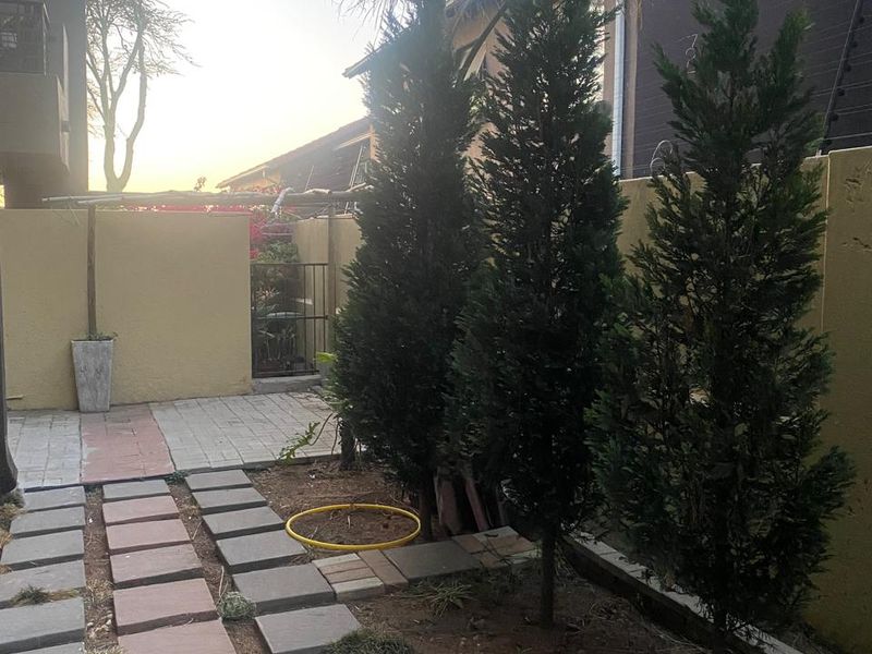 A rear garden area featuring a paved walkway, boundary wall with electric fencing, and established trees.