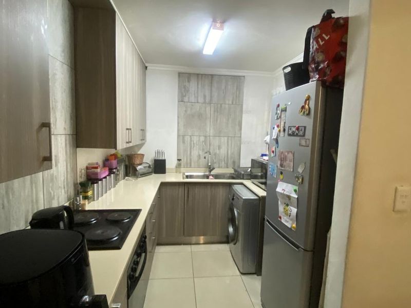 A compact galley-style kitchen featuring modern wood-finish cabinetry, tiled flooring, a built-in electric hob, and an integrated oven.