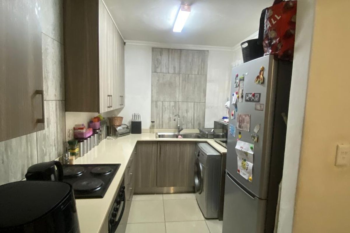 A compact galley-style kitchen featuring modern wood-finish cabinetry, tiled flooring, a built-in electric hob, and an integrated oven.