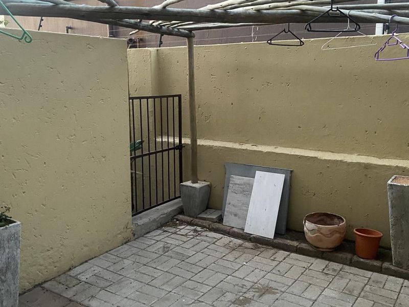 A small, paved rear courtyard area featuring a timber pergola structure and enclosed by a perimeter boundary wall with a security gate.