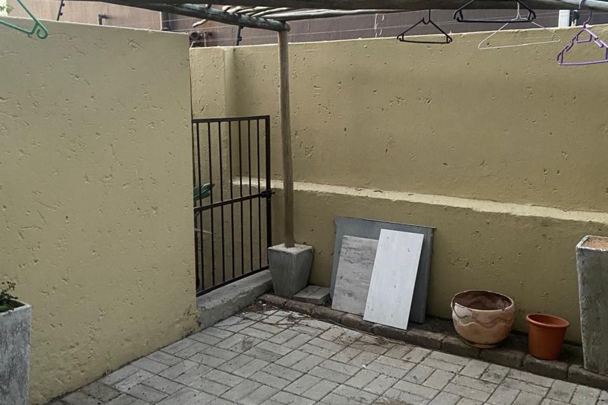 A small, paved rear courtyard area featuring a timber pergola structure and enclosed by a perimeter boundary wall with a security gate.