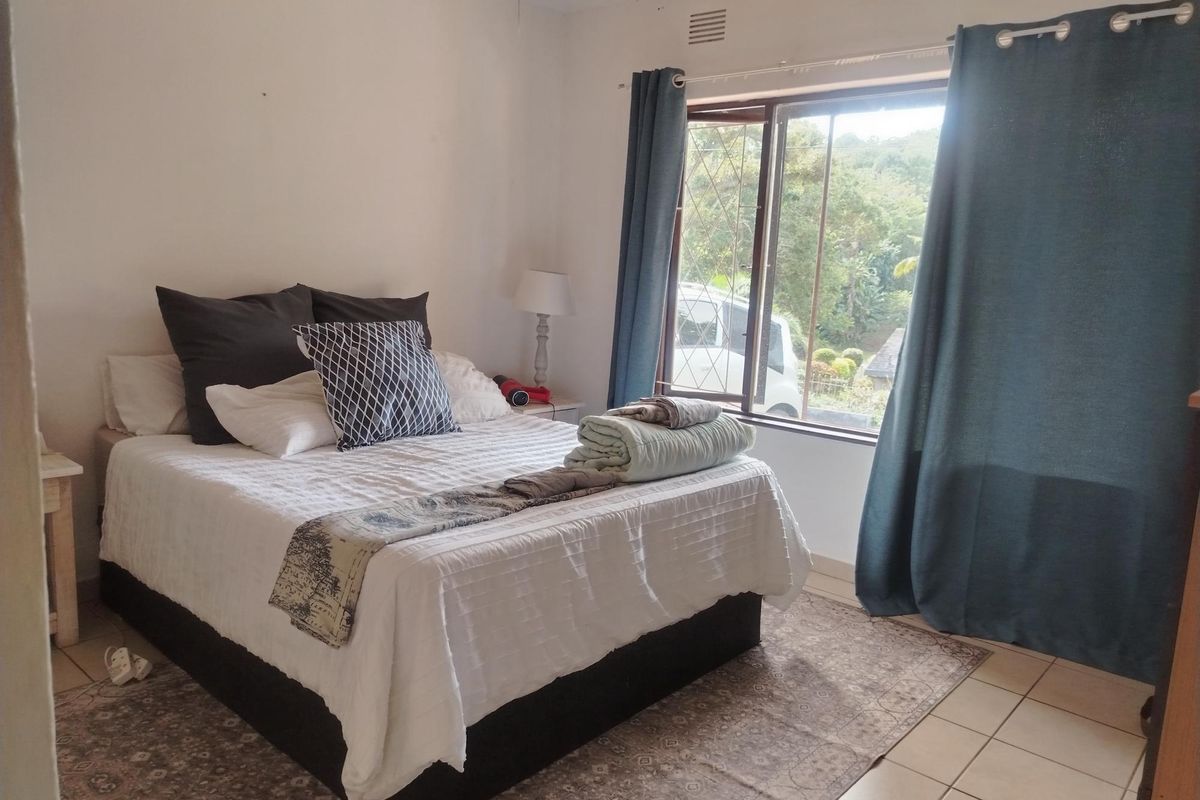 A functional bedroom featuring tiled flooring, a large window with security bars, and built-in ventilation.