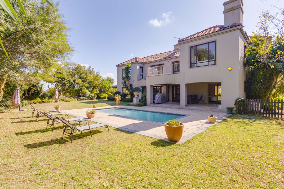 Rear view of a two-story house featuring a swimming pool, paved pool deck, covered patio, and a balcony overlooking the landscaped garden.