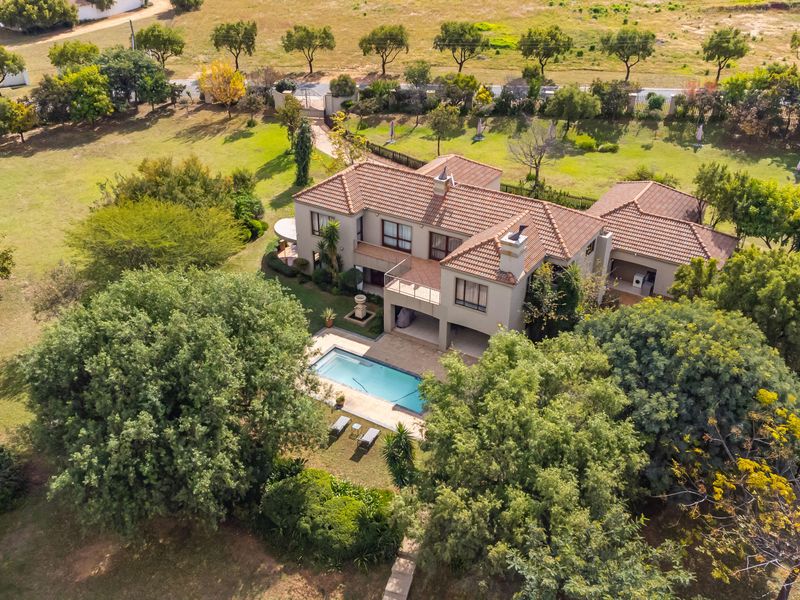 Aerial view of a large residential property featuring a tiled roof, swimming pool, expansive garden, and a balcony overlooking the outdoor area.