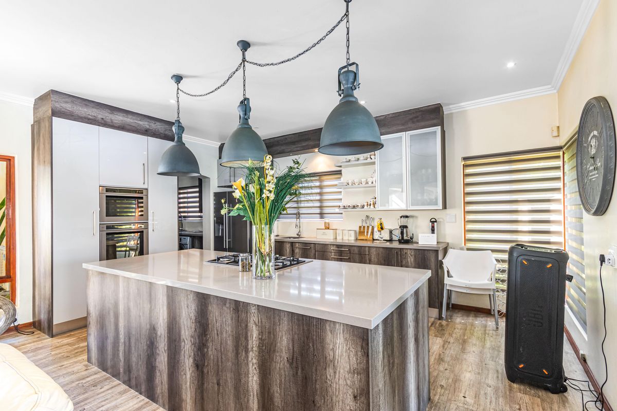 Modern kitchen featuring a large central island with stone countertops, built-in oven, gas hob, and contemporary pendant lighting.