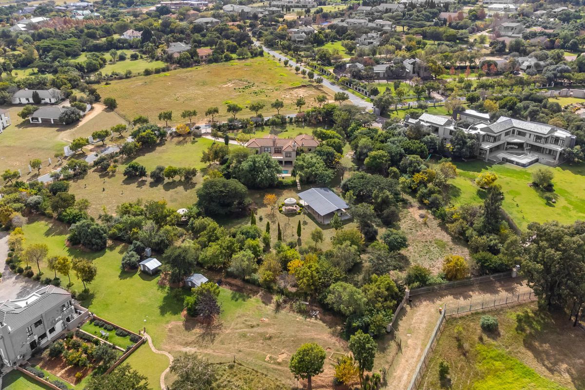 Aerial view of a large residential estate featuring expansive landscaped grounds, mature trees, and multiple structures within a suburban setting.
