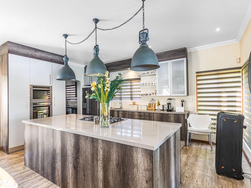 Modern kitchen featuring a large central island with stone countertops, built-in oven, gas hob, and contemporary pendant lighting.